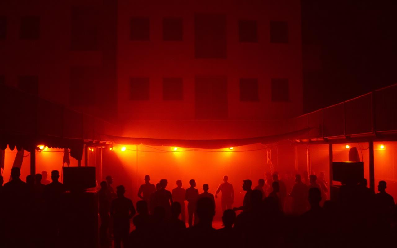 Crowd silhouettes under warm red light at an open-air Accra venue